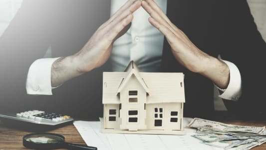 Homme joignant les mains au dessus d'une maquette de maison
