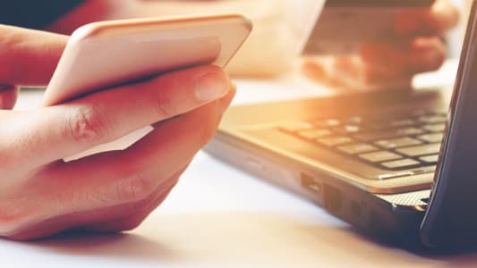 Homme tenant un smartphone et une carte bancaire devant un ordinateur