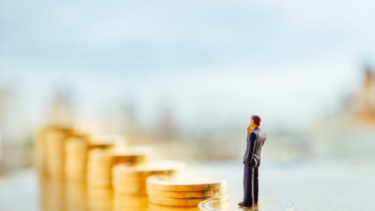 Miniature d'un homme se tenant sur une pile de pices avec la ville en arrire-plan