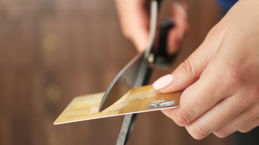Mains coupant une carte bancaire avec une paire de ciseaux