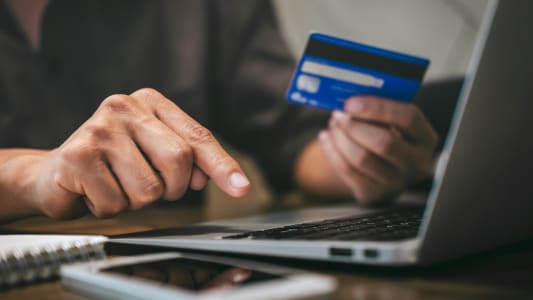 Un homme tient une carte bancaire devant un cran d'ordinateur
