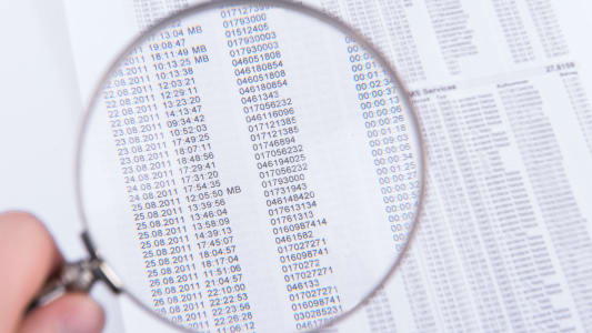 Homme utilisant une loupe pour lire une liste de chiffres