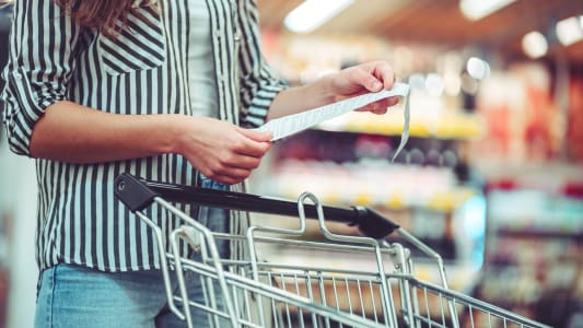 Femme devant un caddie lisant un ticket de caisse