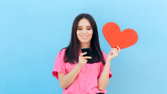 Une femme consulte un smarphone, un coeur dans la main