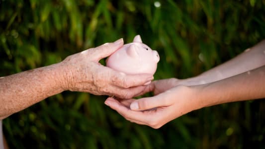 Gros plan de la main d'une femme ge qui transmet une tirelire  une jeune femme
