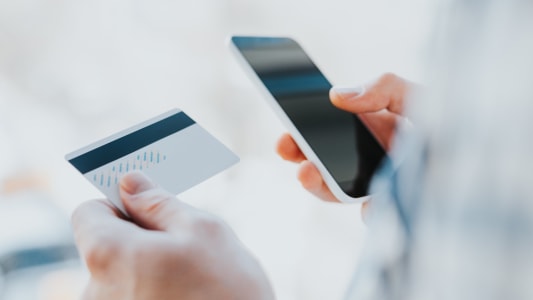 Un jeune homme consulte son mobile et tient une carte bancaire