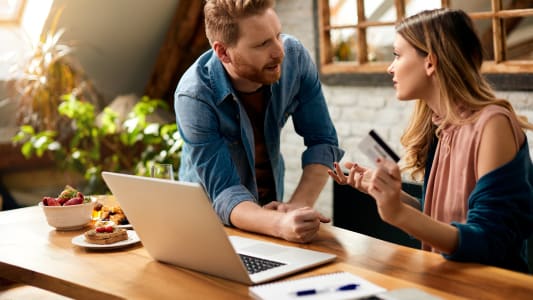Couple discutant devant un ordinateur, carte bancaire  la main
