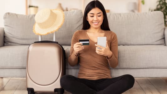 Une femme prépare son voyage une carte bancaire et un mobile à la main