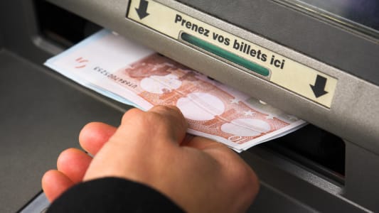 Une main retire des billets d'un DAB