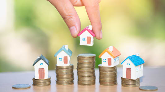 Une main dpose une maison sur une pile de pices