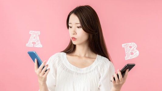 Une femme hésite entre deux téléphones mobiles