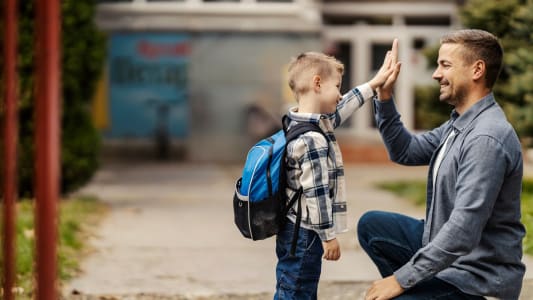 Un pre et son enfant se tapent dans la main devant l'cole