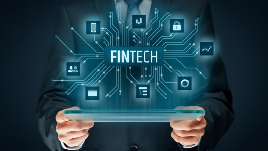 un homme tient une tablette d'o sort l'inscription Fintech avec des symboles.