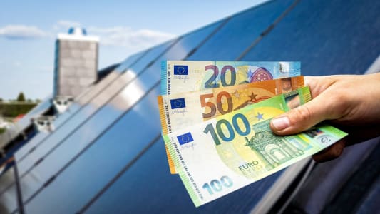 Des panneaux photovoltaques sur le toit d'une maison et une personne tenant des billets.