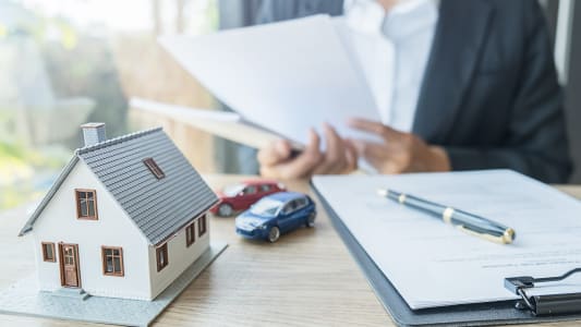 Une femme tient un contrat  ct d'une voiture et maison miniatures