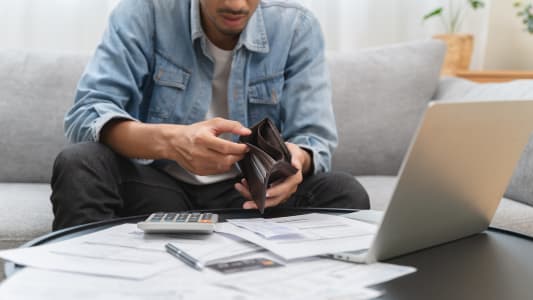 Un homme devant son ordinateur regarde son portefeuille vide.