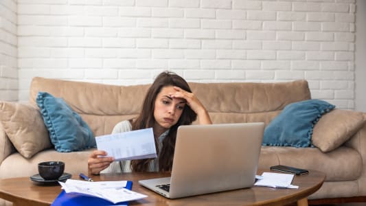Une femme devant son ordinateur regarde des documents en soupirant. 