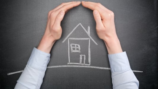 Une maison dessine  la craie protge par des mains.