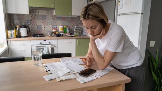 Une femme regarde des factures dans sa cuisine. 