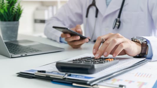Un mdecin devant son ordinateur avec une calculatrice.