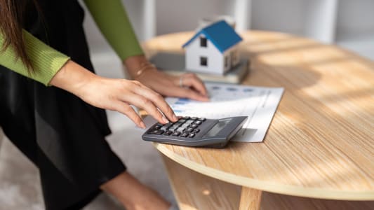 Une maison miniature  ct d'une personne utilisant une calculatrice.