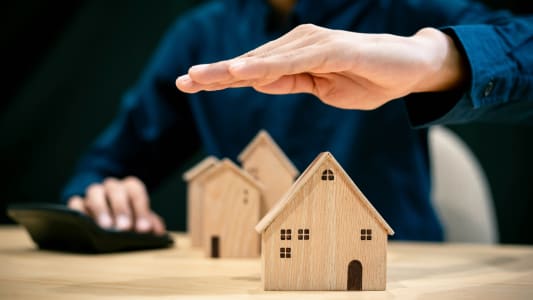 Une personne protge des maisons miniatures avec ses mains.