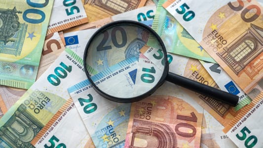 Des billets de banque en euros et une loupe.