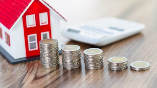 Une maison miniature, une calculatrice et des piles de pices de monnaie.