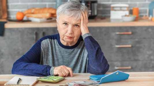 Une femme l'air inquiet avec une calculatrice et des pices de monnaie.
