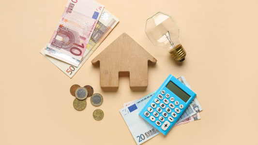 Une maison miniature, une ampoule, des pices de monnaie et billets.