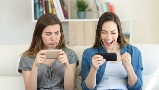 Deux femmes regardent leur tlphone, l'une joyeuse l'autre triste.