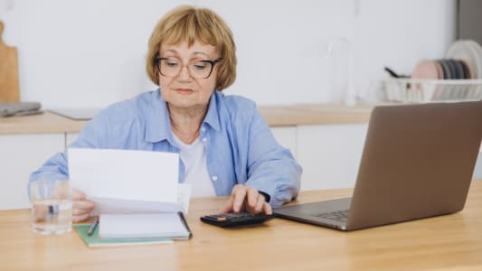 Une femme regarde son ordinateur avec une calculatrice. 