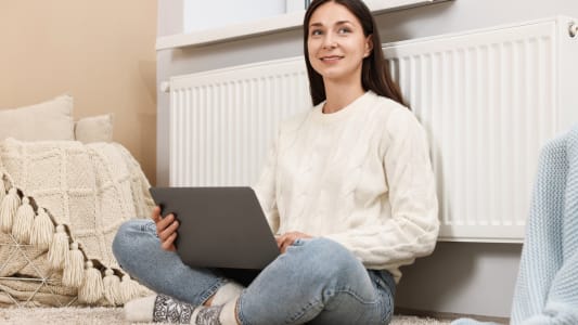 Une femme assise devant son radiateur avec un ordinateur.