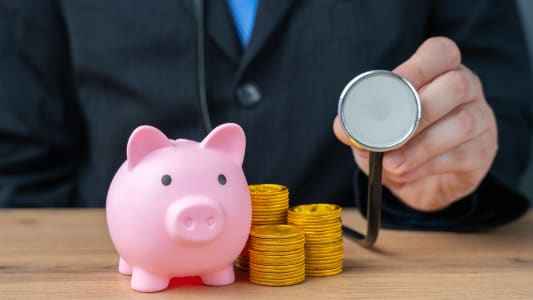 Une tirelire avec des piles de pices de monnaie et un stthoscope.