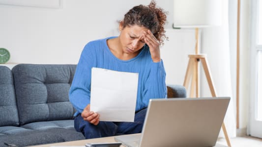 Une femme regarde son ordinateur et des documents l'air préoccupé.