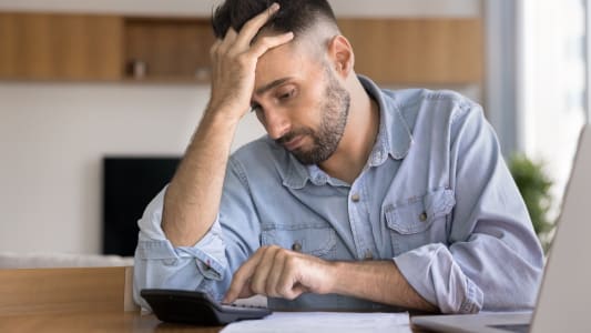 Un homme regarde une calculatrice l'air inquiet.