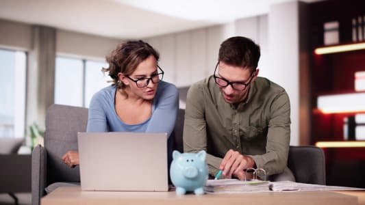 Un homme et une femme devant un ordinateur et une tirelire.