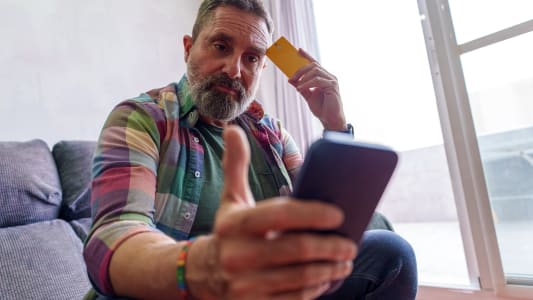 Un homme regarde son tlphone portable et sa carte bancaire.