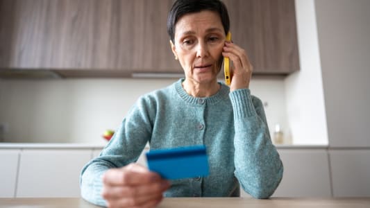 Une femme au tlphone regarde sa carte bancaire.