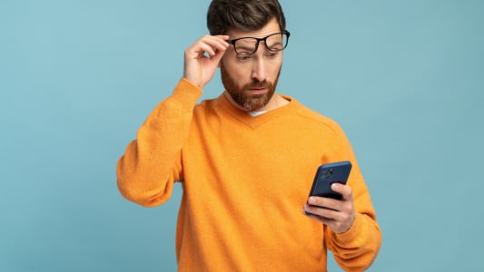Un homme regarde son téléphone l'air surpris.