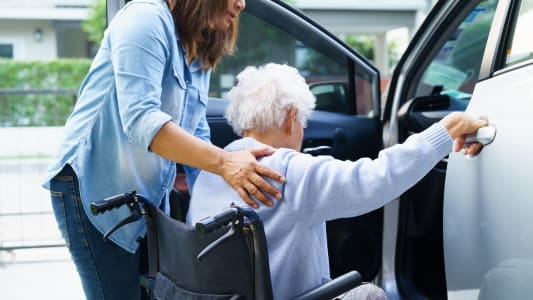 Une femme aide une personne ge  monter dans une voiture.