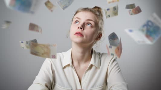 Une femme regarde des billets voler autour d'elle.