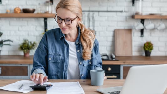 Une femme regarde son ordinateur et des documents.