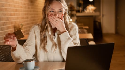 Une femme regarde son ordinateur avec sa carte bancaire l'air inquiet.