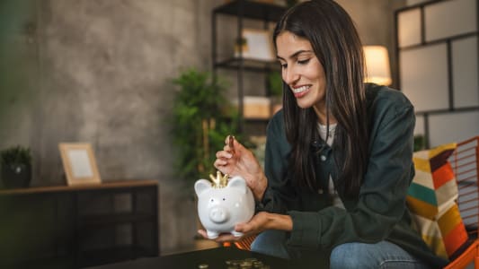 Une femme met de l'argent dans une tirelire.