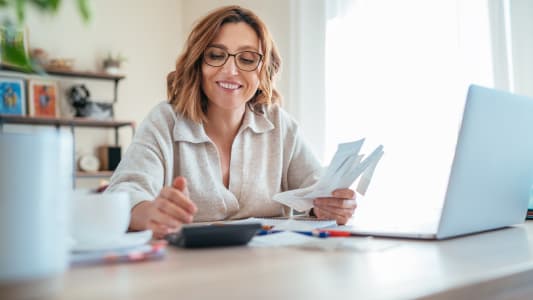 Une femme regarde des documents devant son ordinateur.