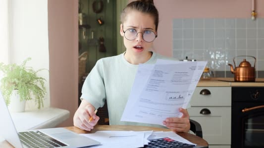 Une femme regarde son ordinateur et des documents l'air surpris.