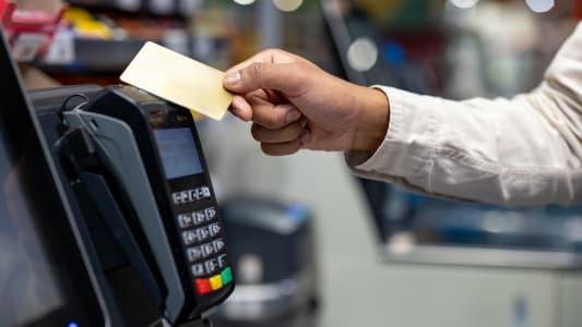 Une main tenant une carte de crdit au-dessus d'un terminal de paiement lors d'un achat dans un magasin. Concept de paiement sans contact.