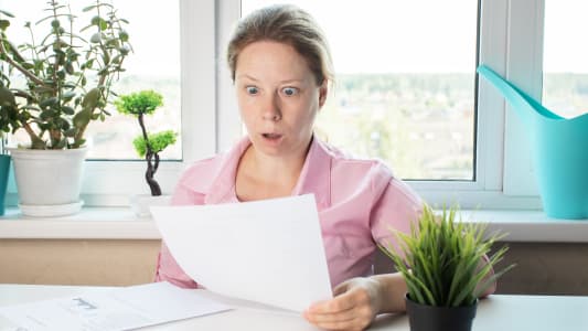 Une femme choque regardant une lettre, examinant des papiers avec des documents bancaires.