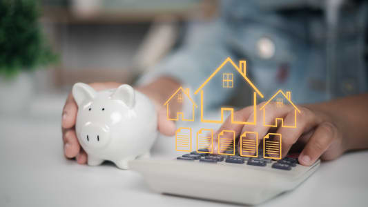 Personne tenant une tirelire et calculatrice, hologramme immobilier.